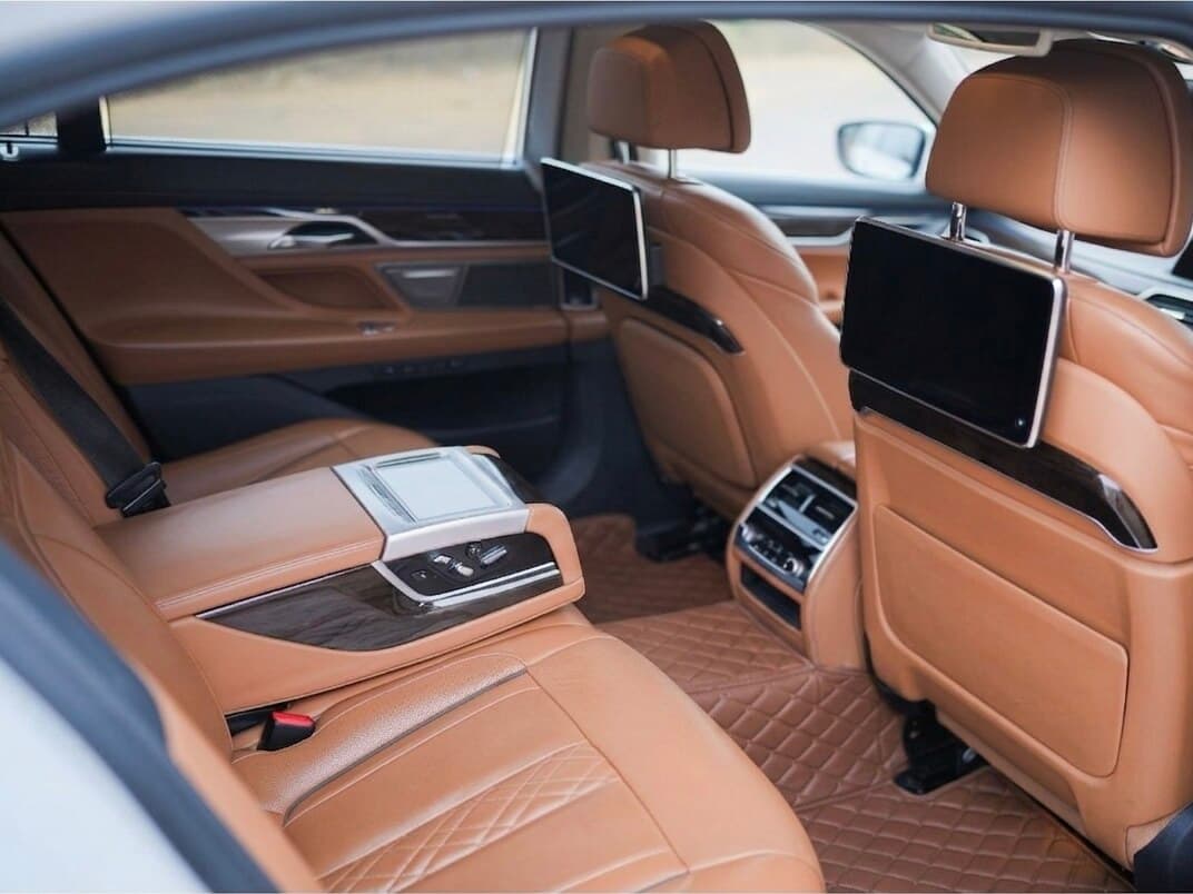 BMW 7 Series rear cabin with cognac quilted leather, dual rear entertainment screens, and rear console controller — premium limousine rental in Bangalore