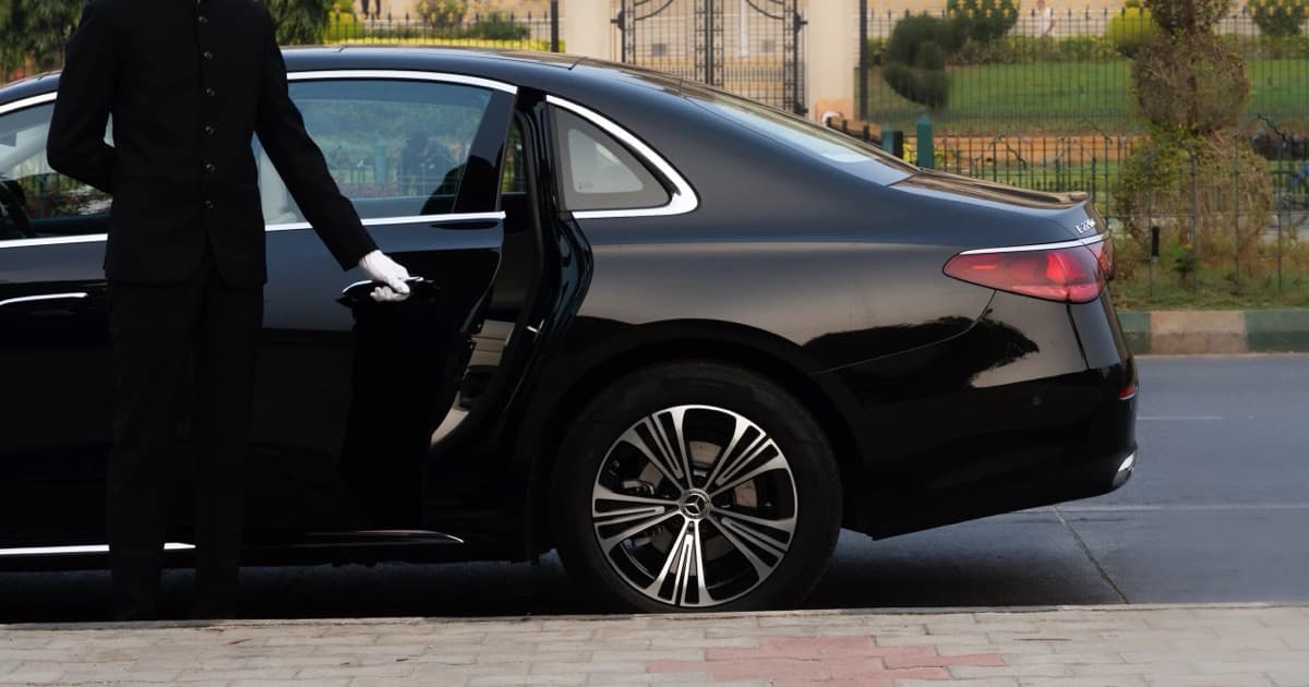Chauffeur-driven luxury car rental in Bangalore. Arista chauffeur opening the rear door of a Mercedes-Benz